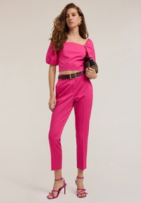 Completo bicolore fucsia composto da un top corto con maniche a sbuffo, pantaloni tapered a vita alta e sandali con tacco a strappo.