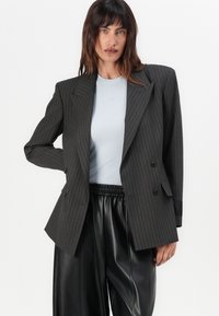 Gestreepte blazer in donkergrijs met een gestructureerd ontwerp, dubbelwaardig knopen en scherpe revers, gecombineerd met een lichtblauwe ribbeltop en zwarte leren broek.