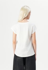 T-shirt en coton blanc à manches courtes et col rond, avec une coupe décontractée et des fentes latérales discrètes, associé à un pantalon large sombre.