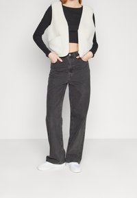 Vitt fleecefoder väst med två framfickor, bärs över en svart långärmad crop top. Kombinerat med högmidjade svarta jeans och vita sneakers.