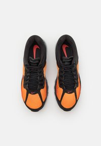 Zapatillas deportivas negras y naranjas con parte superior de malla, que presentan cordones negros, un collar acolchado y el logo de Nike en rojo; diseñadas para comodidad y soporte.