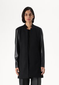 Black coat with a collared design, featuring wool fabric and leather sleeves. The coat is straight-cut, reaching mid-thigh, with no visible fastenings.
