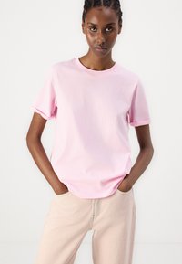Rosa bomull t-skjorte med en avslappet passform, korte rullede ermer og en klassisk rund hals, sammen med lysebeige bukser.
