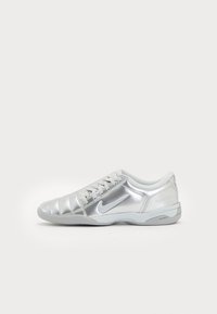 Zapatilla deportiva plateada con un upper metálico elegante, diseño texturizado, cierre con cordones y suela de goma gris. Presenta un sutil detalle de marca.