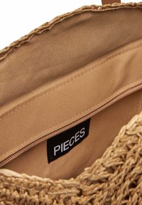 Borsa a spalla in paglia intrecciata con fodera in tessuto color beige e una piccola tasca con zip. Presenta un'etichetta nera con la scritta "PIECES" all'interno.