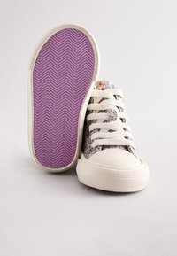 Sneakers in tessuto scintillante con punta in gomma bianca e lacci. La suola è viola con motivo a spina di pesce, che offre una presa texturizzata.