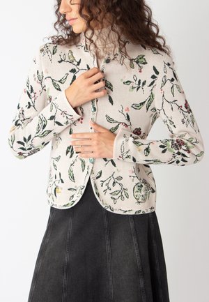 Cardigan en tricot beige clair avec des motifs floraux et d'oiseaux en vert, rouge et jaune. Dispose d'un col rond et d'une fermeture à boutons.