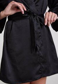 Szatynowy czarny szlafrok z wiązanym paskiem, gładką teksturą i długimi rękawami. Materiał układa się elegancko, z starannie wykończonym dołem.