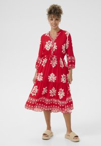 Röd maxiklänning med vita blommönster, V-ringning och trekvartsärmar. Har en tierad design och en sammankrökt midjedetalj.