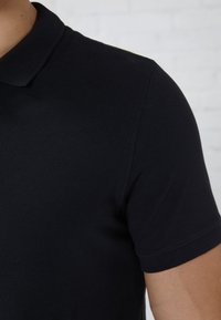 Polo shirt noir en coton texturé, avec un col classique et des manches courtes, doté d'une coupe ajustée pour une apparence épurée.