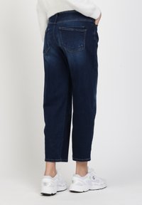 Blauwe denim jeans met een relaxed fit, cropped lengte en achterzakken; gedragen met witte sneakers met lichte accenten en veters.