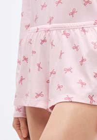 Ροζ σορτς πιτζάμας από απαλό ύφασμα, με ελαστική μέση με κορδόνι και κεντητό σχέδιο μικρών φιόγκων σε πιο σκούρο ροζ.