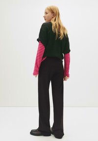 Černé oversized tričko navršené přes růžové a černé pruhované dlouhé rukávy, spárované s širokými černými kalhotami a robustními černými botami.