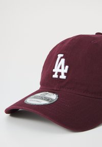 Cappellino da baseball color bordeaux con logo ricamato "LA" bianco, cinturino regolabile e un'etichetta rotonda che dice "9TWENTY ADJUSTABLE" sul visiera.