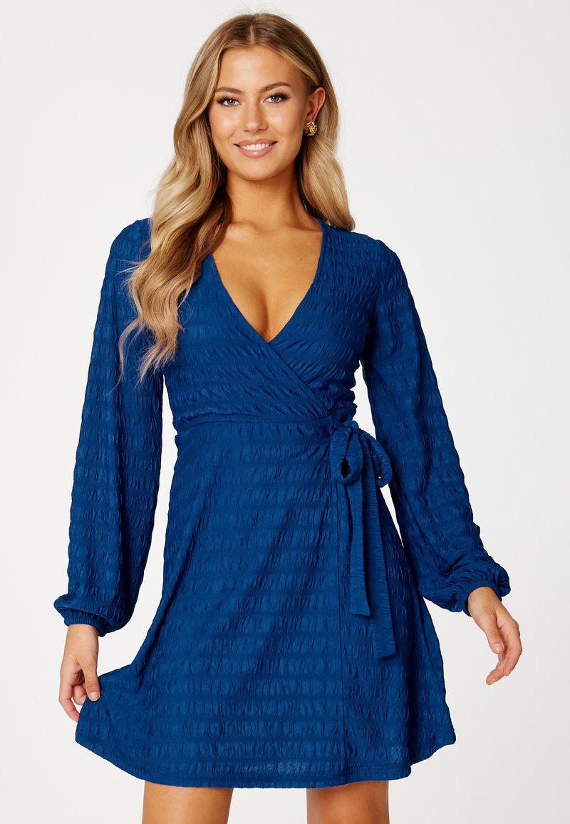 Niebieska sukienka o długości do kolan z długimi rękawami, wykonana z teksturowanej tkaniny, z głębokim dekoltem w serek i wiązanym detalem w talii.