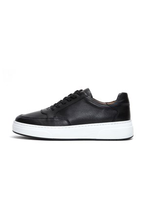 Sneaker en cuir noir avec un bout arrondi, semelle en caoutchouc blanche et six trous pour les lacets. Caractéristiques de la tige texturée et des détails de couture contrastés.