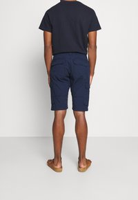 Pantaloni cargo navy con multiple tasche, realizzati in tessuto leggero. Abbinati a una maglietta scura coordinata e sandali casual.