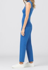 Blå ärmlös topp matchad med blå byxor, med en figurnära design och slät textur. Kompletterad med vita sneakers.