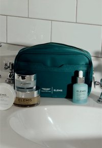 Teal kosmetikkveske med ELEMIS-merkevare, som inneholder fem hudpleieprodukter: to krukker, en flaske og en sirkulær beholder.