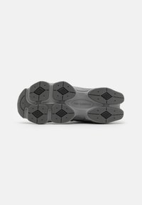 Semelle de chaussure de sport grise avec une surface en caoutchouc texturé, présentant un motif en diamant et le logo "new balance" embossé au centre.