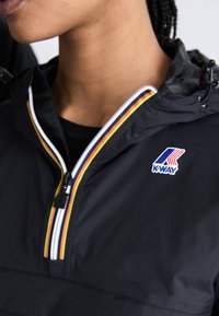 Zwarte jas met een ritskraag, voorzien van een meerkleurige streep en het K-Way-logo. Gemaakt van een gladde, lichte stof.