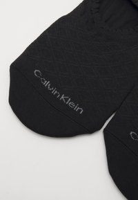 Meias de tornozelo pretas com um padrão diagonal texturizado e topo elástico. Apresenta a marca "Calvin Klein" em cinza no lado.