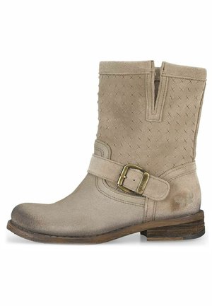 Bota de tobillo de ante color beige con detalle de hebilla, parte superior texturizada con patrones en cruz, puntera redondeada y tacón bajo apilado.