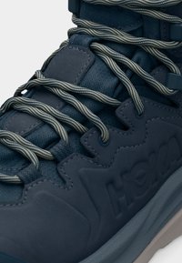 Κοντινό πλάνο ναυτικού μπλε αθλητικού παπουτσιού με χοντρές, ριγέ κορδόνια και ανάγλυφο λογότυπο στο πλάι κοντά στη γκρι σόλα.