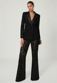 Mustmustreen must-särk, millel on satiinist krae ja laiendatud püksid, esitleb keerukaid pitsimustreid ja kohandatud sobivust.