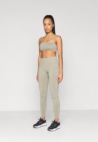 Világosszürke rövid ujjú crop top és magas derekú leggings rugalmas anyagból; a modellen fekete sportcipők vannak fehér talppal.