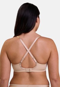 Soutien-gorge beige avec une finition lisse, des bretelles croisées ajustables et un fermoir à crochets. Présente des coutures tonales et un ajustement confortable.