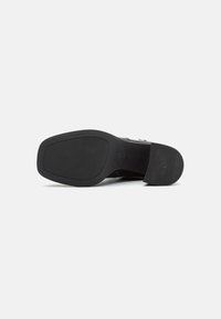 Schwarze Schuhsohle mit einer flachen, strukturierten GummOberfläche. Mit erhöhtem Logo, glatten Kanten und geschwungener Kontur.