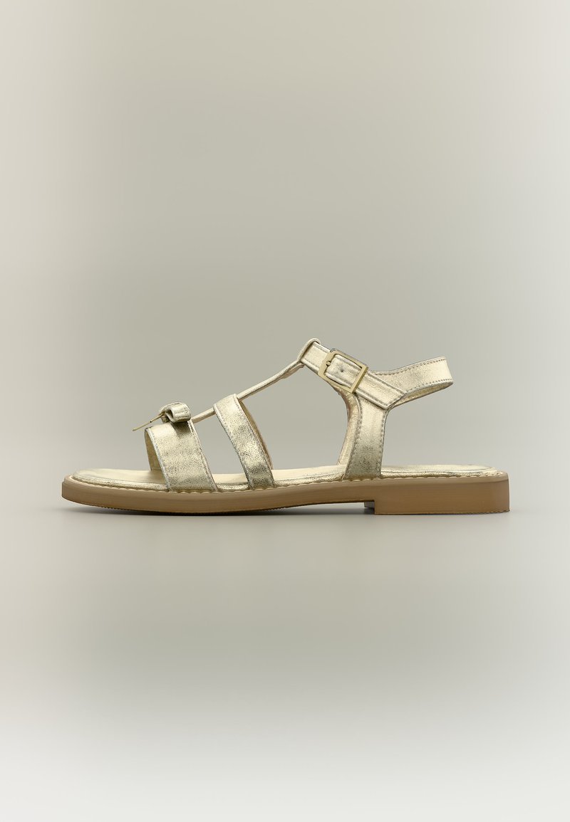 Γυναικεία φλατ σανδάλι με μεταλλικές χρυσές δερμάτινες λουρίδες, ρυθμιζόμενες αγκράφες και ελαφριά καφέ καουτσούκ σόλα.