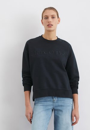 Schwarzer Sweatshirt mit geprägtem „Marc O'Polo“-Logo, Rundhalsausschnitt, lockere Passform und gerippte Bündchen. Wird mit hellblauen Jeans getragen.