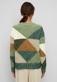 Sweter z dzianiny z geometrycznym wzorem w odcieniach zieleni, kremu, brązu i beżu, z ściągaczem na dole i przy mankietach. Gruby, teksturowany materiał.