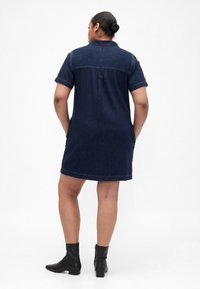 Jeans obleka s kratkimi zavihanimi rokavi, ovratnikom in ravnim silhueto v temno modri barvi, kombinirana s črnimi gležnjarji.