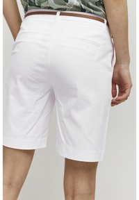 Shorts bianchi in cotone con una trama liscia, dotati di una tasca posteriore e una cintura marrone. Design semplice, vestibilità sartoriale, taglio fino al ginocchio.
