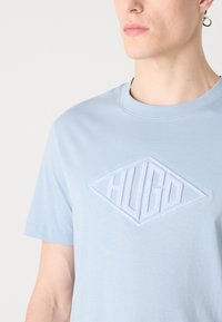 Lyseblå bomull T-skjorte med et diamantformet, teksturert HUGO-logo i hvitt over brystet. Rund hals, korte ermer.