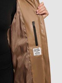 Tan padded jacket interior featuring a zippered pocket and a fabric label with text. Smooth lining and minimal design accents.
