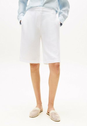 Shorts en lin blanc avec une coupe décontractée, dotés de poches latérales et d'un ourlet roulé. Associés à des mules légères en tissu tressé.