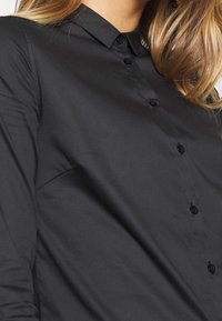 Svart långärmad skjorta med klassisk krage, med knäppt fram och slät yta; tillverkad av ett lätt, vävt tyg.