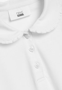 Fehér póló ing fodros gallérral, három szív alakú gombbal és "next SCHOOL" címkével. Puha szövet szerkezet.