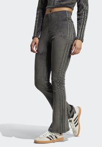 Gray ribbed flared pants feature three stripes down the side, made of soft material with a smooth texture, paired with neutral sneakers.