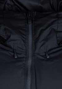 Section de doudoune noire avec une fermeture éclair centrale, des cordons de serrage, un tissu mat lisse et des détails de texture matelassée.