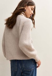 Maglione a maglia spessa in beige chiaro, con una texture a coste e una vestibilità leggermente accorciata. Abbinato a jeans a vita alta.
