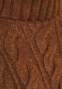 Pletená tkanina svetrové barvy ve stínu tan-hnědé s texturovaným vzorem copánků s vystouplými motivy a žebrovaným límcem, představující měkkou vlněnou texturu.