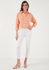 Een oranje en witte gestreepte button-up overhemd met een kraag, opgerolde mouwen, gecombineerd met witte skinny jeans en lichtgekleurde blokhak sandaaltjes.