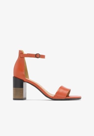 Sandal de cuero naranja de punta abierta con tira en el tobillo y hebilla, tacón de bloque con detalle de grano de madera y suela negra sobre fondo blanco.