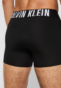 Black boxer shorts made of smooth fabric, featuring a white "Calvin Klein" logo waistband and a snug fit with a mid-thigh length.
