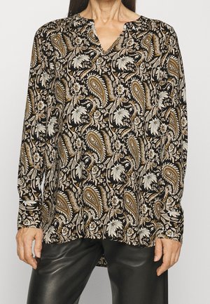Blouse noire à manches longues avec motif floral et cachemire beige et blanc portée avec un pantalon en cuir noir.